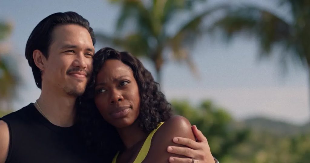A couple, Molly and Andrew, stands closely together outdoors on a sunny day, with palm trees and a soft blue sky in the background. The man, wearing a sleeveless black shirt and a silver chain necklace, has his arm wrapped around the woman’s shoulder, smiling gently as he gazes into the distance. The woman, wearing a yellow tank top, rests against his chest with a thoughtful expression, her eyes also looking ahead. The scene radiates warmth, intimacy, and a sense of peace.
