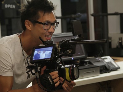 Chinese American director Wesley chan wears glasses and smiles behind the camera as he works on set.