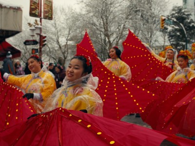 Chinese cultural dancers wearing bright yellow costumes and waving large red flags dance in a snowy parade in Vancouver's Chinatown